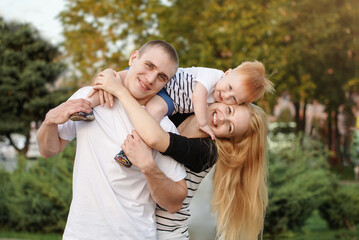 Happy family is playing outdoors in the park in the summer. Dad, mom and son are hugging and laughing together