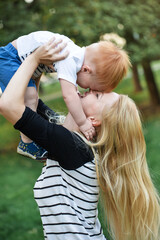 Mom and son are playing together outdoors in the summer. Mother is holding the kid boy and kissing him