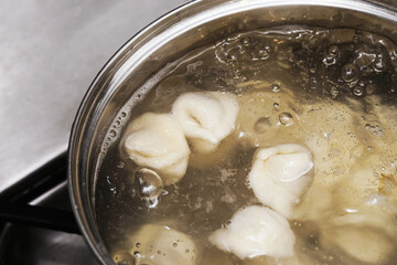 Boiling dumplings in pot on stove. Fresh pierogi cooking in hot water with bubbles. Traditional homemade dough meal preparation in kitchen. Closeup of food during cooking process.