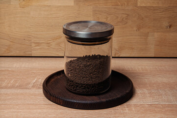 Glass jar filled with dark brown granular material on a wooden surface