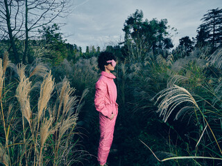 Person in a pink suit stands among tall grasses outdoors, stylish and confident, wearing sunglasses in a natural field setting, highlighting bold fashion. © SHOTPRIME STUDIO