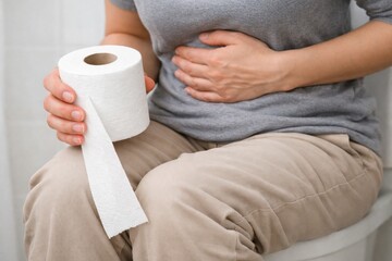 Adult sitting on toilet clutching stomach with toilet paper, illustrating diarrhea, stomach ache, digestive distress, and gastrointestinal health issues
