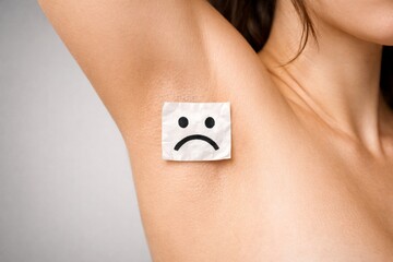 Adult female armpit skin with sad face sticker symbolizing sweating problem, odor concern, hygiene, discomfort and body care concept
