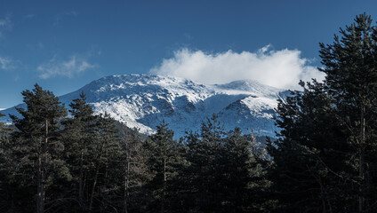 A high-resolution panoramic view of the snow-covered Sierra de Guadarrama mountain range, showcasing the Peñalara peak under a clear blue winter sky