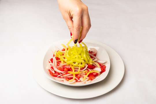 deliciosa ensalada de tomate con cebolla y aj&iacute; esparcido por una mano de mujer sobre la ensalada, todo servido en un plato blanco