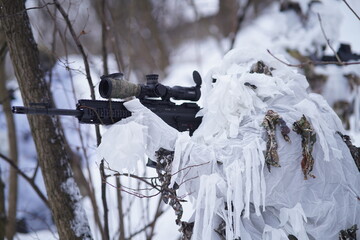 A special forces scout peers through the forest using optics, his white camouflage breaking up his...