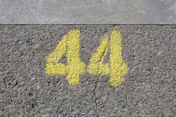 Yellow imprint of the number forty-four on asphalt pavement. Urban texture with worn paint, suggesting frequent use or weather exposure. Hand-painted figures of 4 four and 4 on rough gray background