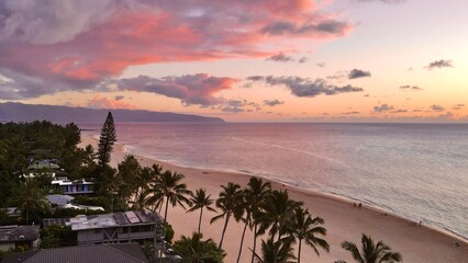 Tropical beach at sunset with palm trees and calm ocean along the Hawaiian coastline, showcasing colorful clouds, peaceful shoreline, and serene island atmosphere