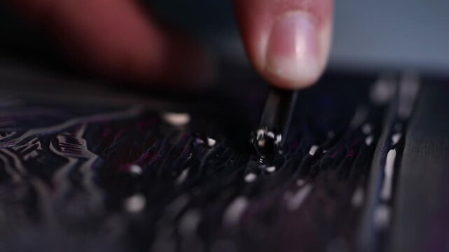 Macro shot of an artist's hands using a gouge to carve intricate details into a linoleum block, creating a relief printmaking matrix in a creative art studio.