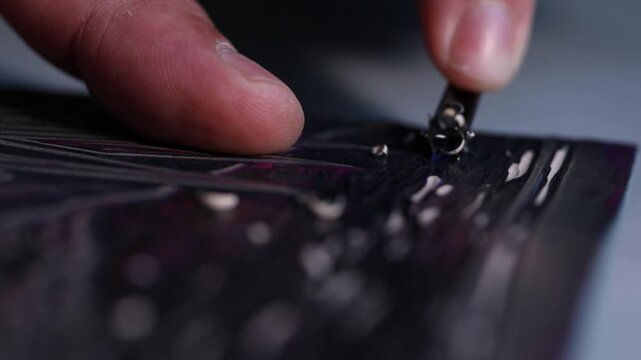 Macro shot of an artist's hands using a gouge to carve intricate details into a linoleum block, creating a relief printmaking matrix in a creative art studio.