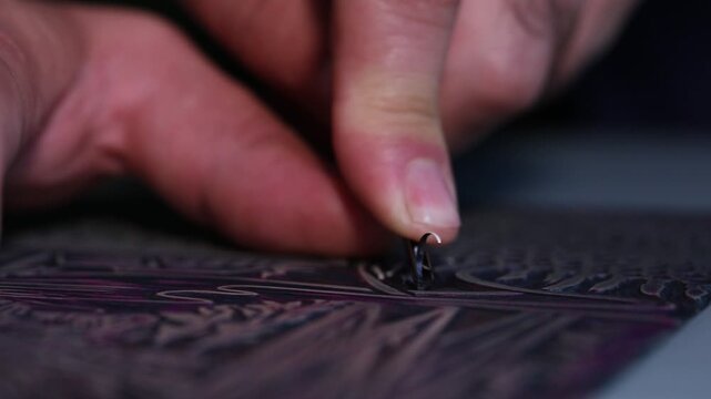 Macro shot of an artist's hands using a gouge to carve intricate details into a linoleum block, creating a relief printmaking matrix in a creative art studio.