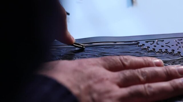 Macro shot of an artist's hands using a gouge to carve intricate details into a linoleum block, creating a relief printmaking matrix in a creative art studio.
