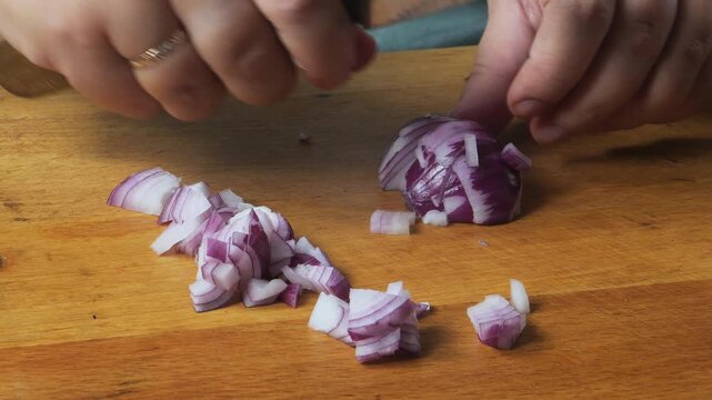 A woman's hands slice a red onion with a knife on a cutting board on the table and place it on a plate. Medium shot.