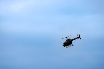 Single helicopter flying at an angle silhouetted against a pale blue sky