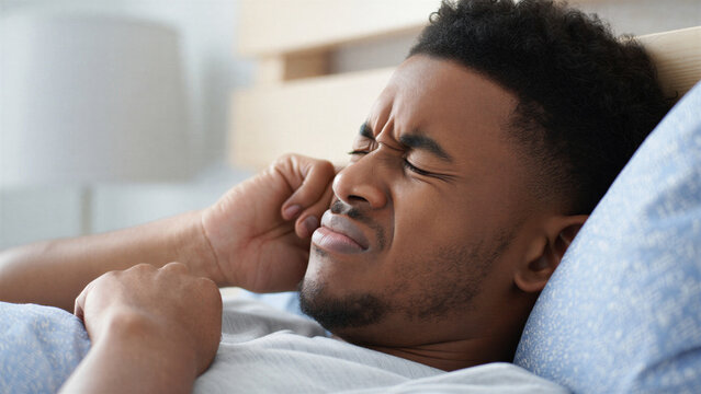 Young man waking up with jaw pain in bed, sleep bruxism discomfort, tmj tmd jaw clenching, morning headache from teeth grinding, facial tension stress, sleep disorder impact