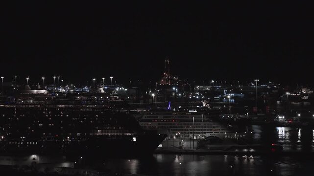 Aerial night scene in Las Palmas, Gran Canaria shows AIDA cruise ships, quay lights, cranes, and an industrial tower, with slow motion and gentle water reflections.