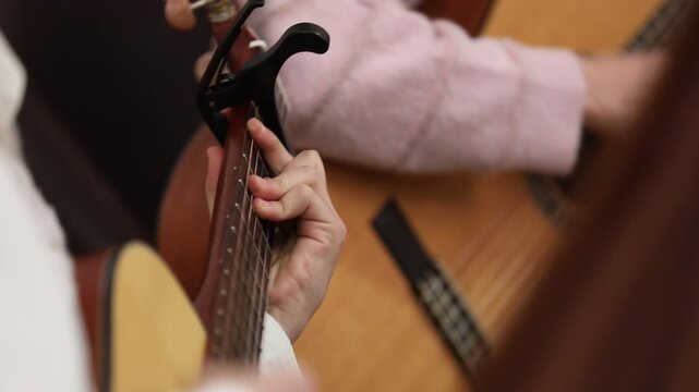 Close-up of musician tuning acoustic guitar using a mobile app on a smartphone screen, ensuring perfect pitch before playing a song during a music lesson.

