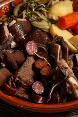 A hearty Portuguese stew with assorted meats, sausages, potatoes, carrots, and greens, traditionally served warm in a rustic bowl.