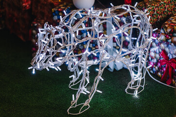Photo of a wire bear, glowing lamps, and garlands in a park for Christmas and New Year's. Design and decor.