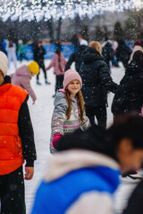 A beautiful happy teenage girl or child skates on a snowy outdoor rink in winter. Photography, portrait, sports, and leisure concept.