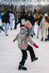 A beautiful happy teenage girl or child skates on a snowy outdoor rink in winter. Photography, portrait, sports, and leisure concept.