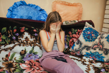 A beautiful girl, a teenage child, lies on a bed at home with a smartphone, closing her eyes in fear, playing on the gadget, experiencing horror.