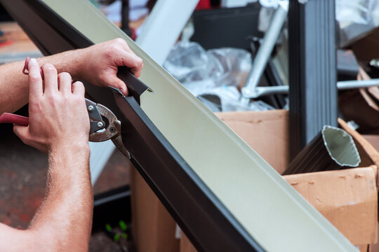 Metal worker uses tools to cut gutter channels metal trim in busy workshop with tools materials.