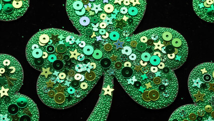 Green sequin shamrock decorations on a black background. St Patrick's Day lucky clover symbol with beads and stars texture