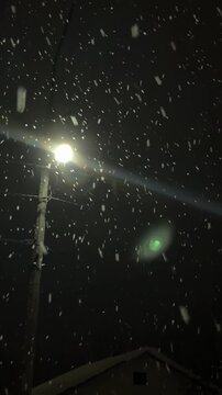   A captivating shot of heavy, dense snowflakes falling rapidly at night. The snow is brightly lit by the sharp, concentrated light of a street lamp, creating a beautiful contras