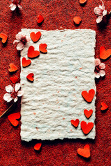 Top view of rough fiber paper frame with scattered paper hearts and spring flowers for holiday card design.