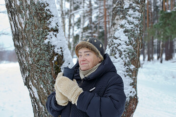 Portrait of a smiling elderly woman holding a cup of coffee in a winter park.