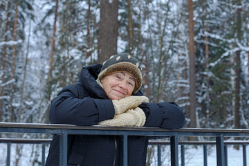 A smiling elderly woman in a winter public park. Winter outdoor recreation for the elderly.
