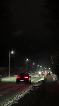 Evening street in winter. It is snowing at night, traffic is full of cars. A captivating shot of heavy, dense snowflakes falling rapidly at night. The snow is brightly 