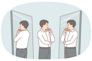 Business man looks in mirror trying on new formal clothes and touches chin with smile