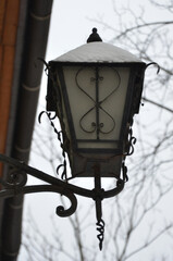 Closeup snow covered  antique metal and glass winter lantern hanging on the external wall of building .