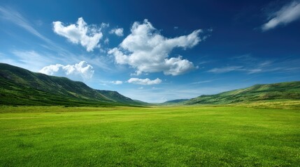 Obraz premium Expansive Green Field Under Bright Blue Sky with Fluffy White Clouds and Rolling Hills in Scenic Landscape View