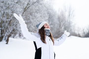 Happy woman enjoying snowfall with raised arms outdoors in winter park
