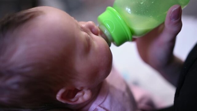 Adorable newborn baby peacefully drinking milk from a feeding bottle held by a caring parent. This tender moment captures the innocence and tranquility of early infancy and parental love