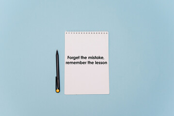 A blank notepad with a motivational quote written in bold text. A black pen lies beside it on a light blue background.