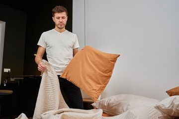 Man standing in bedroom and arranging pillows and blanket on bed