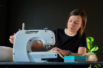 Woman sewing fabric using sewing machine at table with textile materials