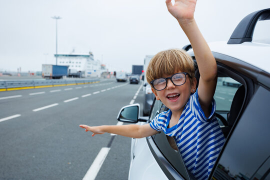 Boy waving happily outside car window wait for ferry boarding