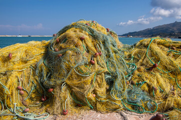 Fishermans equipment lying on the coastline in harbor, heap nylon yellow tangled fishing net in sunlight