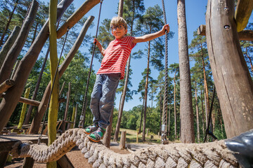 Child balance confidently on rope at forest summer playground
