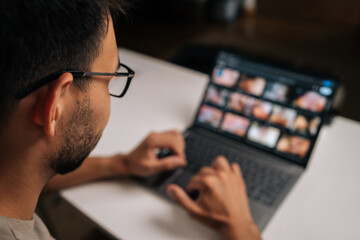 Back view of man in eyeglasses navigating laptop touchpad during video conference, highlighting remote working technology and digital connectivity. Concept of remote working on distance workplace.