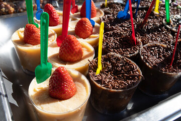 Several cups filled with Brazilian sweets, some made with dark chocolate covered in chocolate sprinkles and others with a coconut base. Each cup has a small spoon on top and a strawberry
