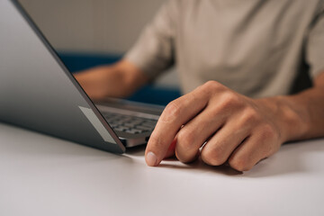 Close-up cropped shot of male freelancer wearing casual clothing working remotely on laptop computer in home workspace, representing digital nomad lifestyle with ergonomic comfort