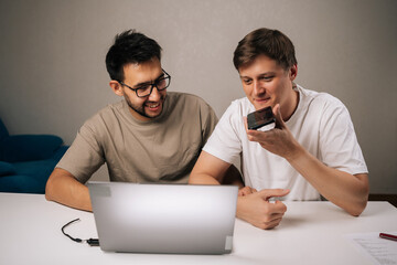 Portrait of two young start-up men in office collaborating on startup plan, using smartphone for calls and messages, sharing ideas, planning strategy and driving innovation and growth.