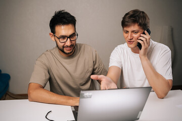 Portrait of two two young startup men brainstorming startup ideas, collaborating ona new business project, using laptop and smartphone for communication and strategy in modern home office.