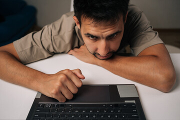 Tired young man working late at office, focusing intently on laptop screen, embodying dedication and commitment to completing important project before deadline.